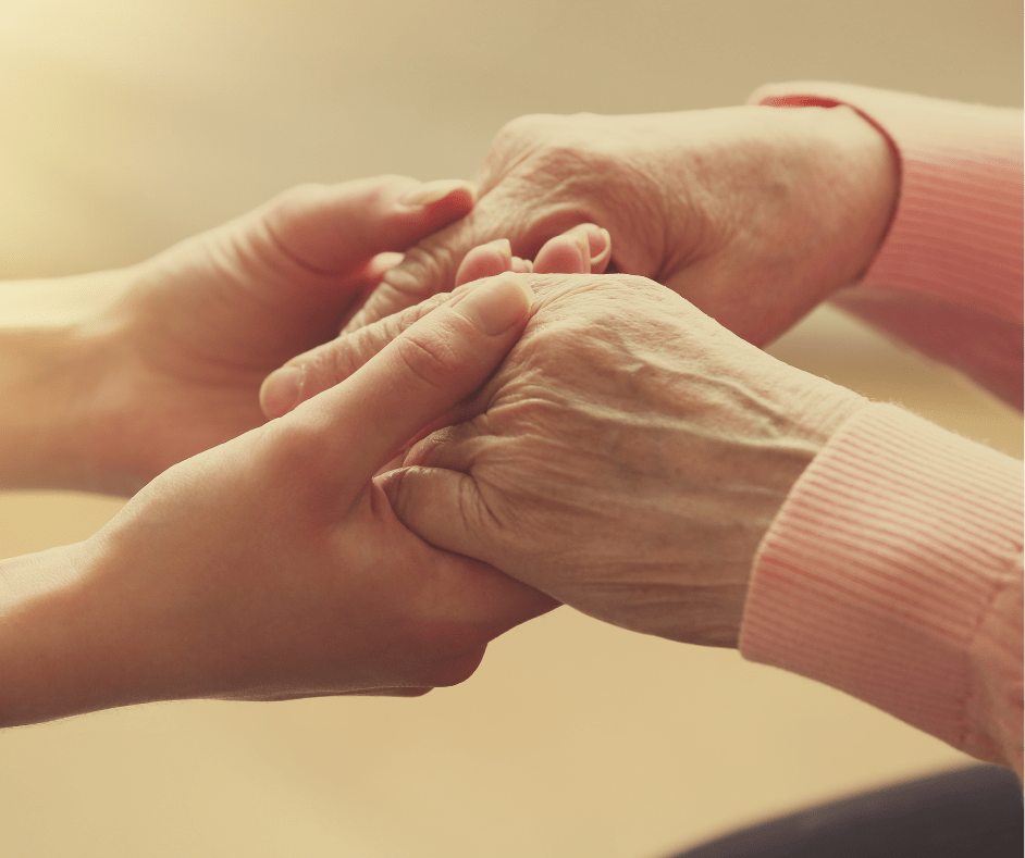 Caregiver holding an older adult's hands during compassionate in-home care.