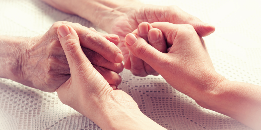 Caregiver holding an older adult's hands while providing compassionate in-home care and support.