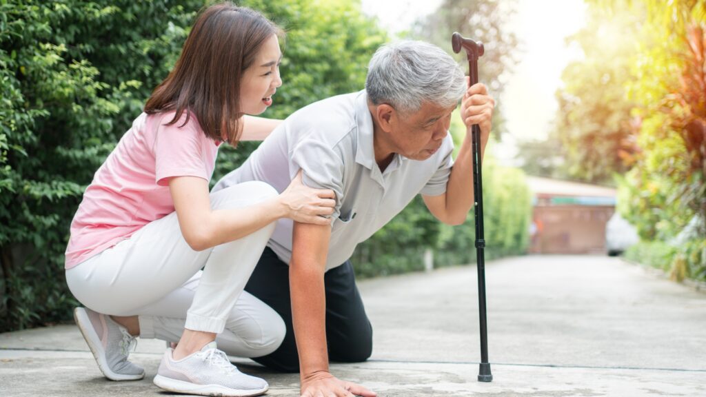 Caregiver helping an older adult regain balance while using a cane outdoors.