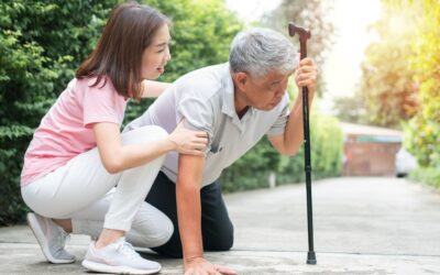 Caregiver helping an older adult regain balance while using a cane outdoors.
