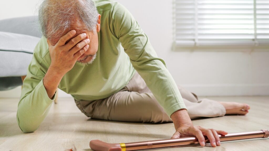 Older adult on the floor after a fall reaching for a walking cane at home.