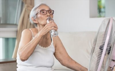 Older adult drinking water while staying cool with a fan during hot weather.