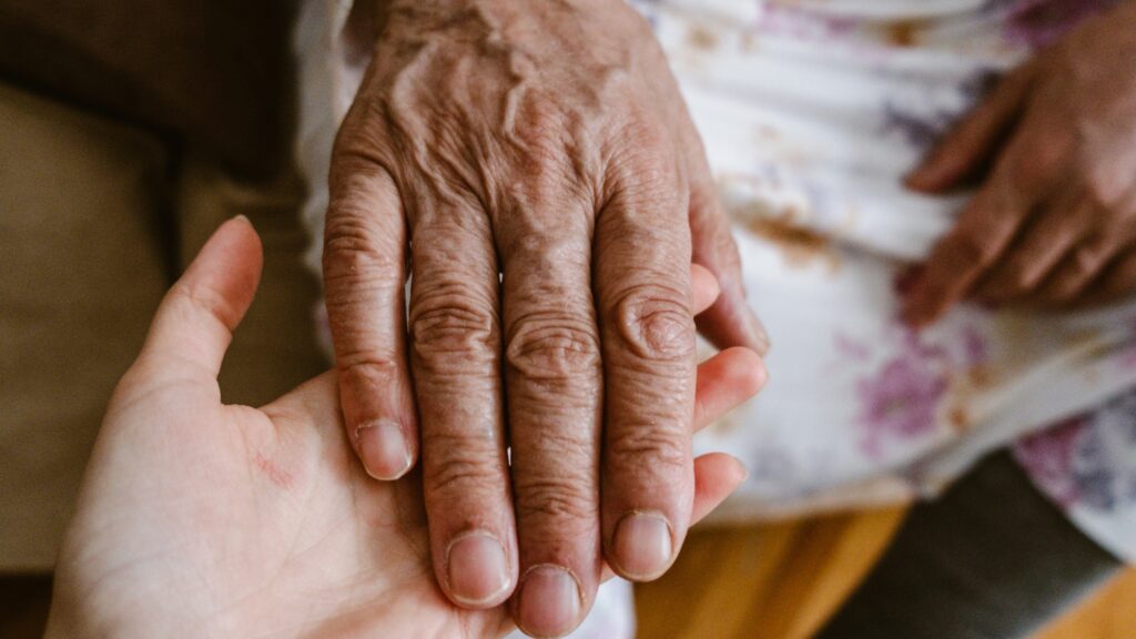 Caregiver holding an older adult's hand to provide compassionate in-home care support.