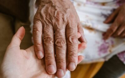 Caregiver holding an older adult's hand to provide compassionate in-home care support.