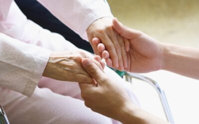 Caregiver holding an older adult's hands during post-hospital recovery at home.